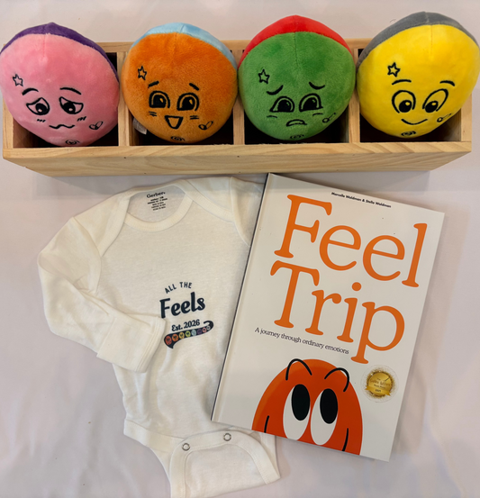 Set of colorful emotion plush dolls, a baby onesie with "All the feels - Est. 2026", and a children's book titled 'Feel Trip' on a white background.